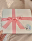 White gift box with a pink ribbon held by a hand on a beige background