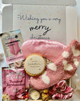 Christmas gift box with pink socks, cookies, and snacks on a white background with festive lights.