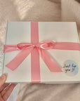 A comforting ‘Thinking of You’ package filled with thoughtful treats and self-care items, such as tea, pamper items, a bracelet, and a handwritten note, neatly arranged in a gift box
