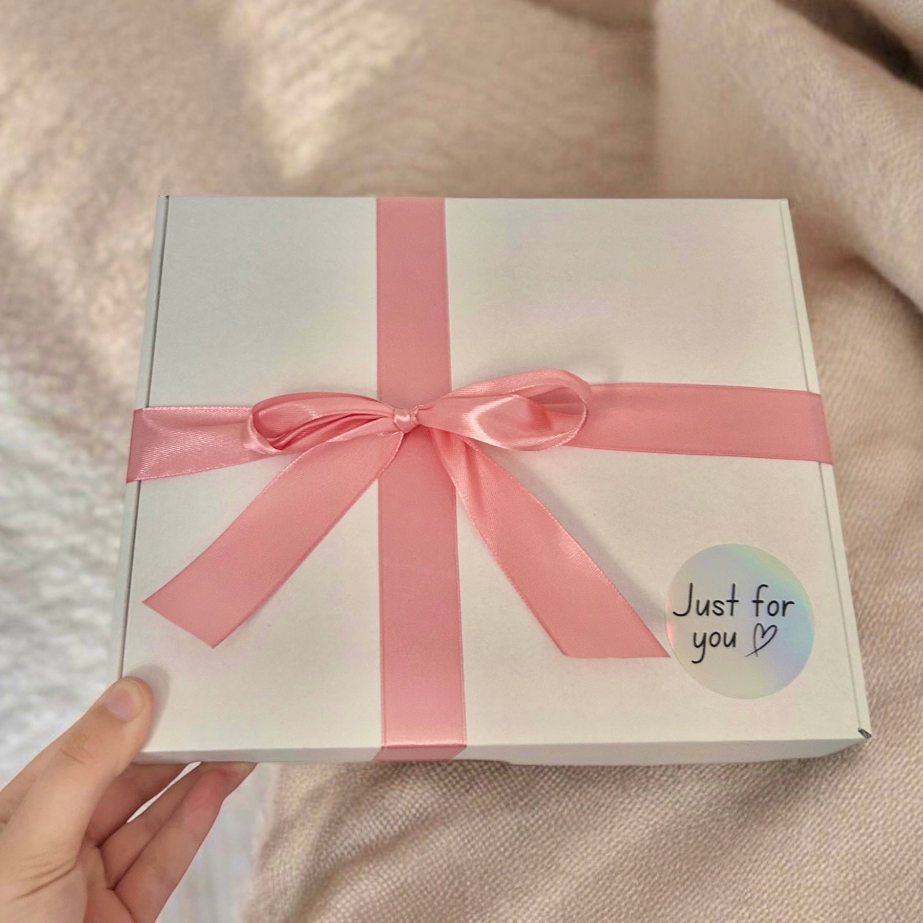 White gift box with a pink ribbon held by a hand on a beige background