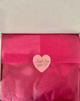 Pink gift bag with 'Just for you' heart-shaped tag in an open box, surrounded by pink flowers.